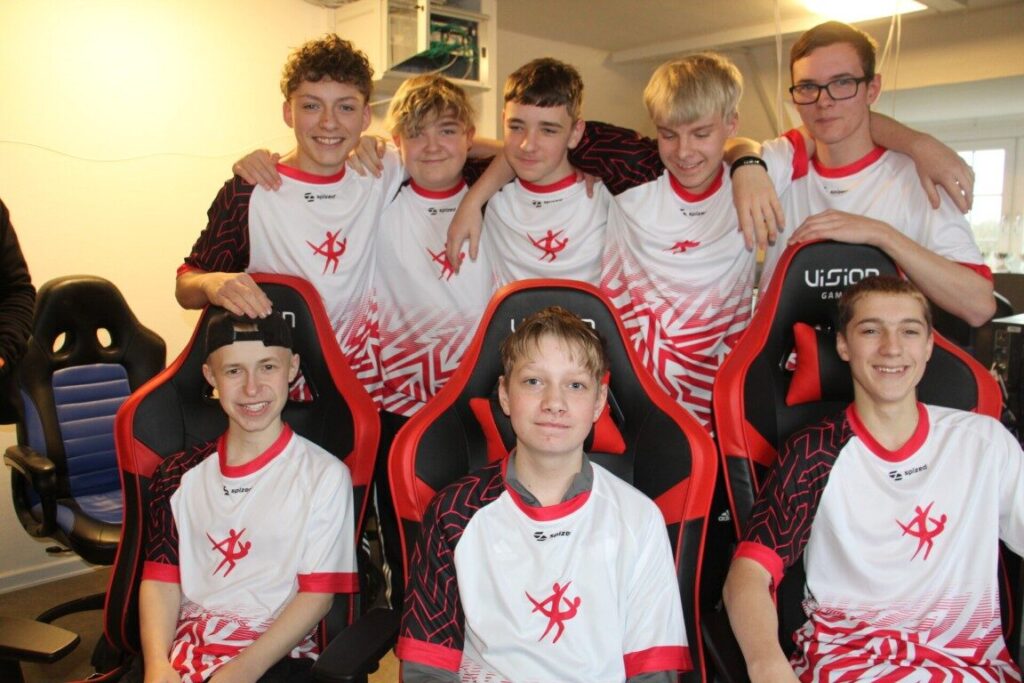 Glade elever i spillertrøjer samlet ved gaming-stolene – stærkt fællesskab på tværs af linjer på en ordblindevenlig efterskole